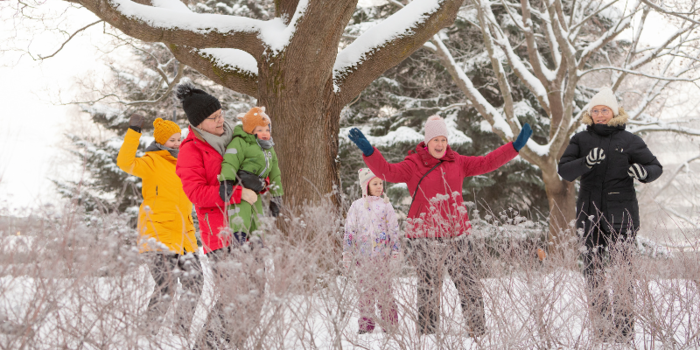 Eri ikäisiä henkilöitä värikkäissä talvivaatteissa ja päähineissä iloitsemassa lumisen talvisessa säässä.