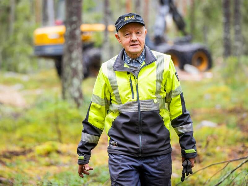 Matti Juva metsässä taustalla metsäkone.