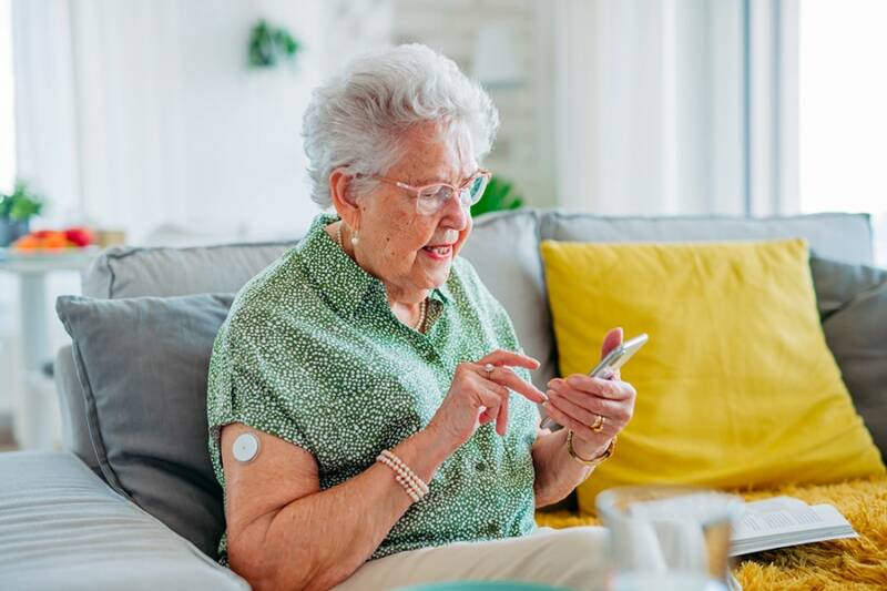 Iäkäs diabetesta sairastava nainen istuu sohvalla ja tutkii puhelintaan.