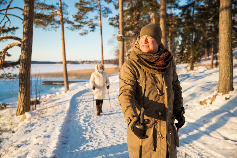 Kaksi naista kävelee taurinkoisessa talvimaisemassa kävelysauvojen kanssa.