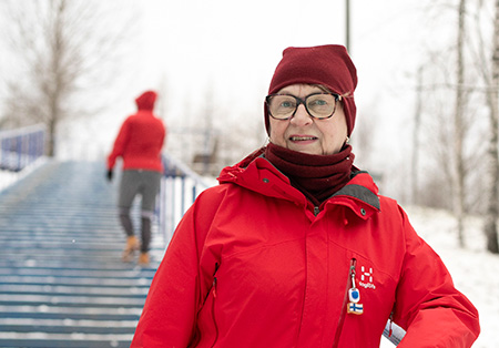 Nainen seisoo talvisilla portailla punaisissa ulkoiluvaatteissa