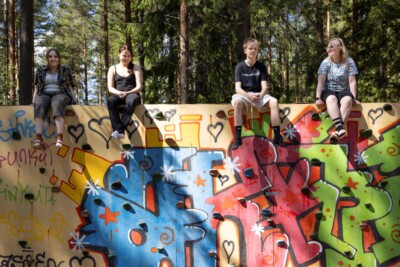 Neljä nuorta istuu auringonpaisteessa graffittiseinän harjalla