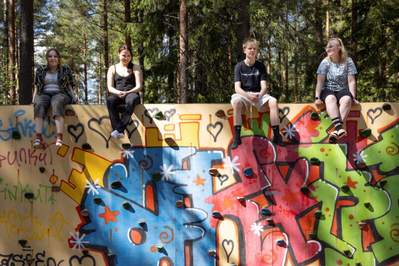 Neljä nuorta istuu auringonpaisteessa graffittiseinän harjalla