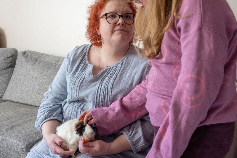 Sanna Puhakka pitää marsua sylissään ja katsoo marsua silittävää tytärtään