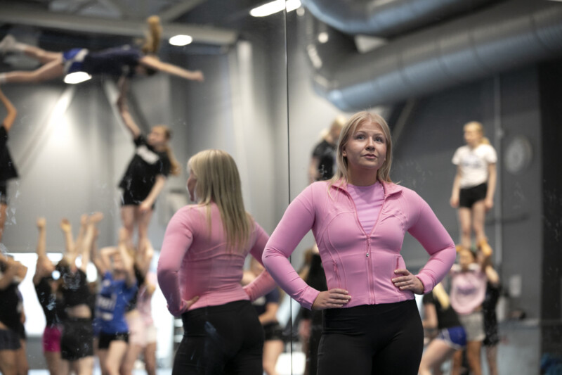 Jenna Maäki poseeraa taustallaan cheerleading-harjoituksissa olevia nuoria