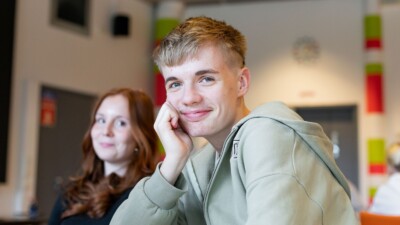 Nuori poika nojaa käteensä ja katsoo kameraan hymyillen
