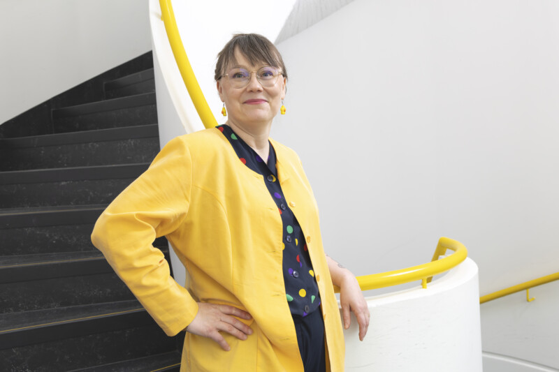 Kirsi-Maria Hytönen seisso portaikossa pukeutuneena keltaiseen bleiseriin