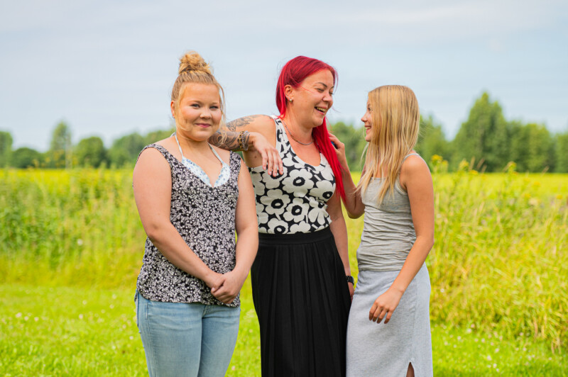 Silja, Salla ja Anna hymyilevät toisilleen niityn laidalla