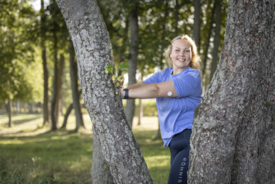 Linda Niemi nojautuu puuta vasten ja hymyilee kemaraan
