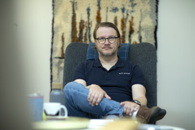 Teemu Ollikainen istuu jalat ristissä ja katsoo kameraan.